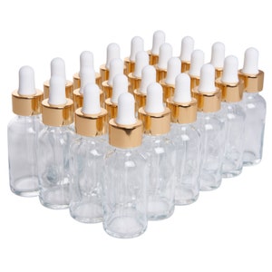 May include: A group of 24 clear glass bottles with gold lids and white dropper tops. The bottles are arranged in a rectangular pattern.