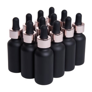 May include: A group of 12 black glass bottles with rose gold lids and droppers. The bottles are arranged in a triangular shape.