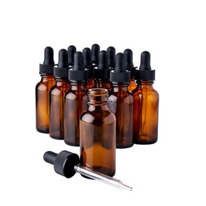 May include: A group of 12 amber glass bottles with black dropper caps. The bottles are arranged in a triangular shape with one bottle in the front and two bottles in the back. A single dropper is lying on the white surface.