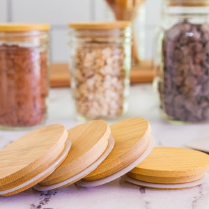 Könnte beinhalten: Vier runde Holzdeckel mit weißen Silikonringen. Die Deckel sind übereinander gestapelt. Die Deckel sind aus natürlichem Bambus.