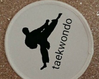 May include: White round patch with a black silhouette of a person performing a taekwondo kick. The text "taekwondo" is written vertically on the right side of the patch.