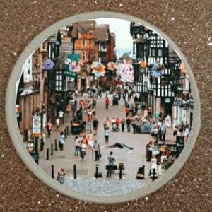 Op de afbeelding: Een zwart-witfoto van een straatbeeld in een Europese stad. De straat is omzoomd door gebouwen met zwart-witte vakwerkconstructies. Er lopen veel mensen op straat. De foto is genomen vanuit een hoog standpunt, met uitzicht op de straat.