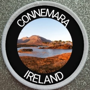 Könnte beinhalten: Ein runder weißer Patch mit einem schwarzen Kreis in der Mitte. Der schwarze Kreis hat einen weißen Rand und die Worte "Connemara Ireland" in weißer Schrift. Im Inneren des schwarzen Kreises befindet sich ein Foto eines Sees und von Bergen in Connemara, Irland.