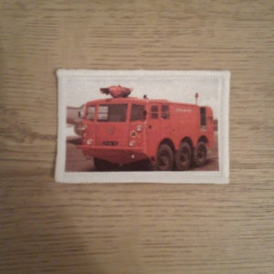 Puede incluir: Un camión de bomberos rojo con una cabina blanca y una escalera blanca en la parte superior. El camión tiene una placa de matrícula negra que dice "17415".