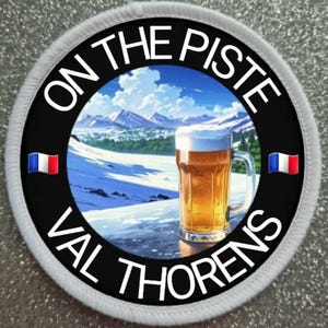 Op de afbeelding: Een witte en zwarte ronde patch met de tekst "On the Piste Val Thorens" rond de rand. Binnen de cirkel is een cartoonafbeelding van een besneeuwde berg scène met een glas bier op de voorgrond. De Franse vlag bevindt zich aan beide zijden van de cirkel.