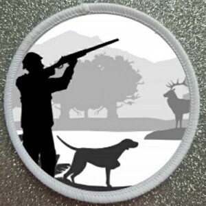 Può includere: Una silhouette in bianco e nero di un cacciatore che mira a un cervo con un fucile in un ambiente boschivo. Un cane bianco e nero è in piedi in primo piano.