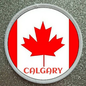 Op de afbeelding: Ronde witte patch met een rode Canadese vlag en het woord "CALGARY" in rode letters.