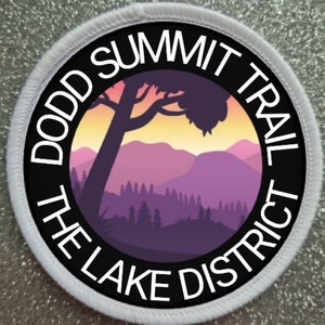 Puede incluir: Un parche circular blanco con texto negro y una silueta de una cordillera de montañas con un árbol en primer plano. El texto dice "Dodd Summit Trail The Lake District".
