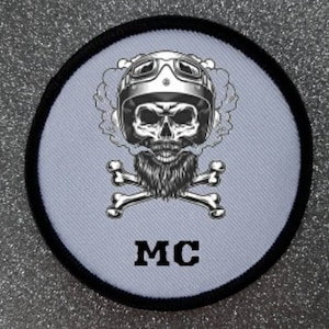 Puede incluir: Parche redondo con borde negro. Representa una calavera con casco y gafas de moto, con barba y humo alrededor. Debajo, huesos cruzados y las letras "MC" en la parte inferior.