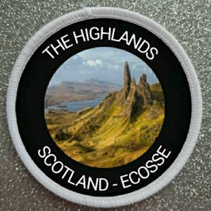 May include: White round patch with black border and a photo of a rocky landscape with a lake in the distance. The text "THE HIGHLANDS SCOTLAND - ECOSSE" is printed in white around the photo.