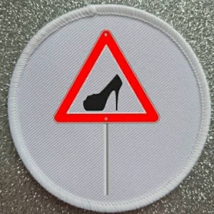 Peut inclure: Patch rond blanc avec un panneau de signalisation triangulaire rouge. Le panneau contient une chaussure à talon haut noire à l'intérieur. Le panneau est sur un bâton blanc.