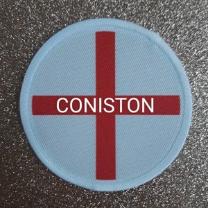 May include: A white and red round patch with a red cross and the word "CONISTON" in the center.
