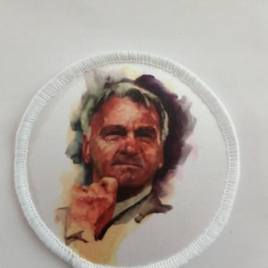 May include: A white round patch with a white border. The patch features a watercolour painting of a man with grey hair and a serious expression. He is wearing a light-coloured shirt and tie.