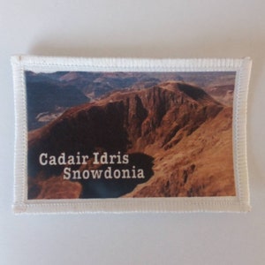May include: A white patch with a photo of a mountain range and the text "Cadair Idris Snowdonia" printed in white.