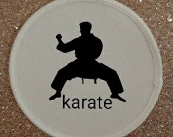 Op de afbeelding: Een witte, ronde patch met een zwart silhouet van een karateka in een vechthouding. Het woord "karate" staat eronder in het zwart gedrukt. De patch heeft een witte, gestikte rand.