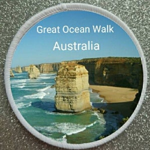 May include: A white round patch with a photo of the Twelve Apostles rock formations along the Great Ocean Walk in Australia. The text "Great Ocean Walk Australia" is printed in white on a blue sky background.