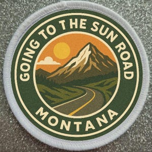 Puede incluir: Parche circular con el texto "GOING TO THE SUN ROAD MONTANA" que rodea una escena de montaña con una carretera sinuosa, el sol y nubes. El parche tiene un esquema de color verde y naranja con un borde blanco.