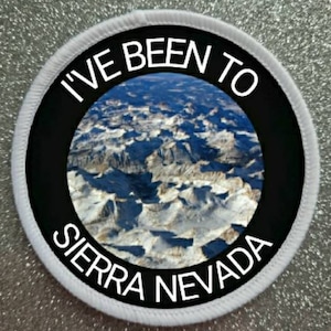 Puede incluir: Parche redondo blanco con un círculo negro en el centro. El círculo negro tiene texto blanco que dice "I've Been To Sierra Nevada" y una foto de una cordillera.