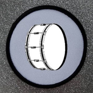 May include: A white bass drum with black hoops and a white background. The drum is surrounded by a black circle.
