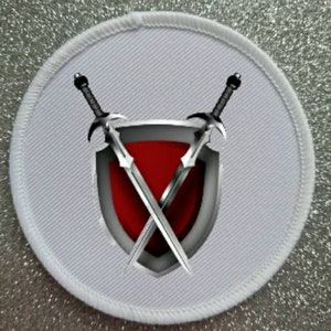 Könnte beinhalten: Weißer runder Patch mit einem roten und silbernen Schild mit zwei gekreuzten Schwertern.