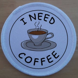 May include: White round patch with black text that reads "I NEED COFFEE" and a cartoon image of a steaming cup of coffee on a saucer.