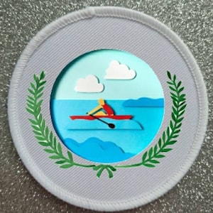 May include: White round patch with a green laurel wreath border. Inside the wreath is a blue circle with a white cloud, a blue sky, and a red boat with a person rowing.