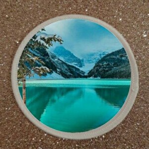 Può includere: Una vista panoramica di un lago turchese circondato da montagne innevate. Il lago riflette il cielo e le montagne, creando un bellissimo riflesso.
