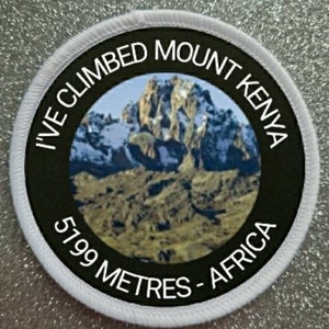 May include: Circular patch with the words "I'VE CLIMBED MOUNT KENYA" and "5199 METRES - AFRICA" in white. The centre shows a mountain scene. The patch has a black background and a white border.