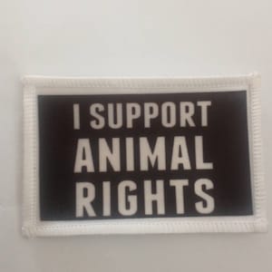 Könnte beinhalten: Weißer Patch mit schwarzem Rand und weißem Text, der "Ich unterstütze Tierrechte" lautet.