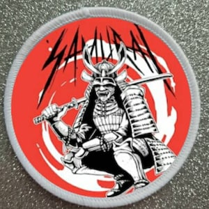 May include: Round patch featuring a samurai warrior in black and white against a red background. The word "SAMURAI" is written in black above the warrior. The patch has a white border.