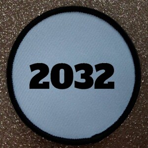 Könnte beinhalten: Runder weißer Patch mit schwarzem Rand und der Nummer 2032 in Schwarz gedruckt.
