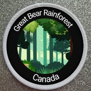 Peut inclure: Un écusson rond avec une bordure noire et une bordure blanche. Il présente une scène de forêt dans des tons verts et bleus, avec les mots "Great Bear Rainforest" et "Canada" en blanc.
