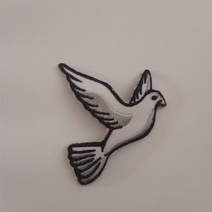 May include: White embroidered dove patch with black outlines and a yellow beak. The dove is flying with its wings spread out.