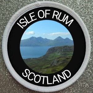 Op de afbeelding: Een ronde witte en zwarte patch met de tekst "Isle of Rum Scotland" en een foto van een landschap met bergen en water.