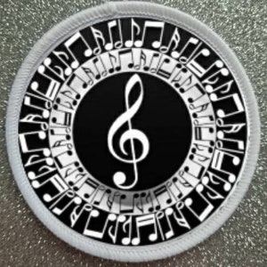 Op de afbeelding: Een ronde witte en zwarte patch met een vioolsleutel in het midden, omringd door een cirkel van noten.