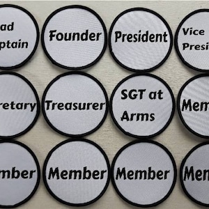 Könnte beinhalten: Zwölf weiße runde Patches mit schwarzen Rändern und Text. Der Text auf den Patches lautet: Road Captain, Founder, President, Vice President, Secretary, Treasurer, SGT at Arms, Member, Member, Member, Member, Member.