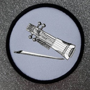 May include: A white and gray embroidered patch of a sarangi, a stringed musical instrument, with a bow. The patch is circular and has a black border.