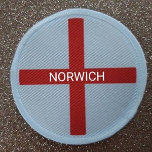 May include: A white and red round patch with a red cross and the word "NORWICH" in the centre.