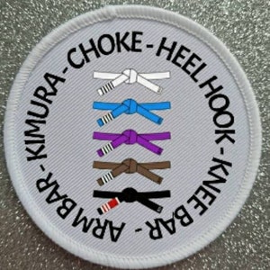 Puede incluir: Un parche redondo blanco con texto negro que delimita un círculo. El texto dice "Arm Bar - Knee Bar - Heel Hook - Kimura - Choke". Dentro del círculo hay seis cinturones de diferentes colores atados en un nudo.