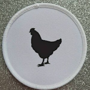 Könnte beinhalten: Runder Stoff-Patch in Weiß mit einer schwarzen Silhouette eines Huhns.