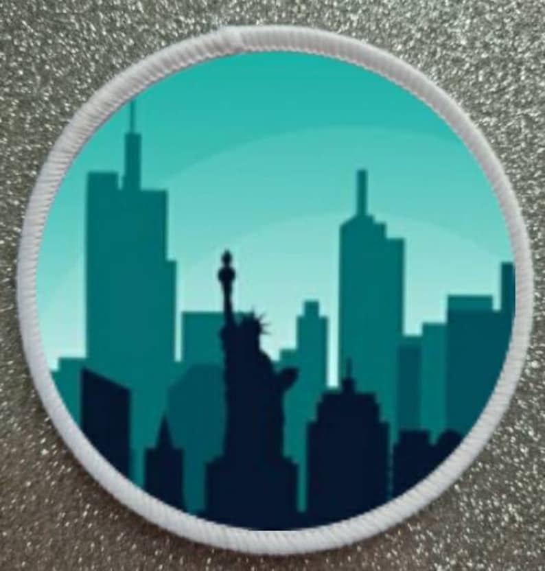 Peut inclure: Un patch rond bord&eacute; de blanc avec un fond bleu turquoise repr&eacute;sentant une silhouette de l'horizon de New York, y compris la Statue de la Libert&eacute;.