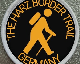 Peut inclure: Un patch circulaire noir et blanc avec une bordure blanche. Le patch représente un randonneur jaune avec un sac à dos et un bâton de marche. Le texte "THE HARZ BORDER TRAIL GERMANY" est écrit en jaune autour du randonneur.