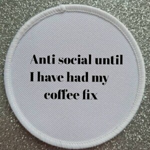 May include: White round fabric patch with the text "Anti social until I have had my coffee fix" in black.