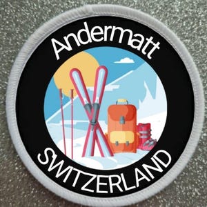 Puede incluir: Un parche redondo blanco y negro con el texto "Andermatt Suiza" en blanco. El parche presenta una ilustración de dibujos animados de una escena de montaña con esquís, bastones de esquí, una mochila y botas de esquí.