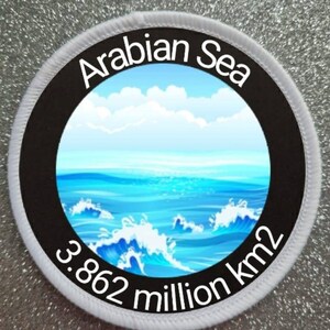 Peut inclure: Un écusson rond blanc et noir avec les mots "Arabian Sea" et "3.862 million km2" imprimés dessus. L'écusson présente une illustration bleue et blanche de vagues océaniques.