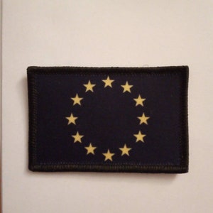 May include: A black patch with a circle of twelve yellow stars on a dark blue background. The patch has a black stitched border.
