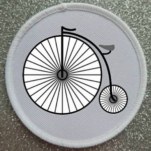May include: A white fabric patch with a black and white illustration of a penny-farthing bicycle.