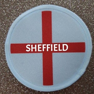 May include: A white and red round patch with the text "SHEFFIELD" in the centre. The patch features a red cross on a white background, resembling the flag of England.