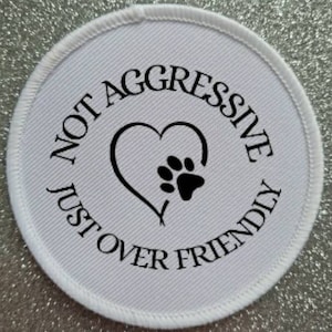 May include: White round patch with black text that reads "Not Aggressive Just Over Friendly" with a paw print inside a heart.