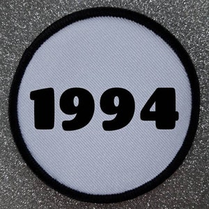 May include: White round patch with a black border and the year 1994 printed in large black letters.